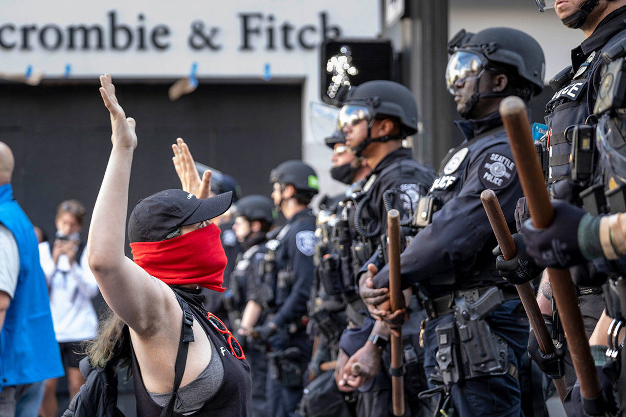 A woman kneels in front of officers Monday in Seattle as peaceful protests took place across the city. (Dean Rutz/The Seattle Times via AP)