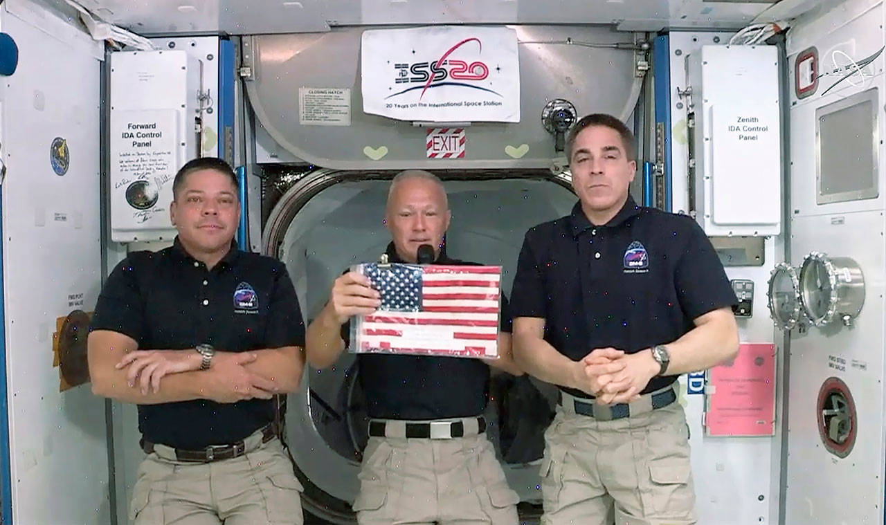 NASA astronauts Robert L. Behnken (left) and Chris Cassidy (right) listen as commander Douglas Hurley speaks Monday about retrieving the American flag left behind at the International Space Station nearly a decade ago. (NASA via AP)