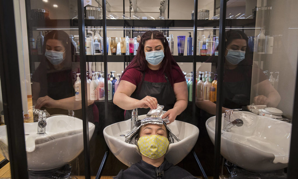 Glass partitions separate hair washing stations as Emily Lothchomphou removes foil wraps from Waan Bartlett’s hair at Salon Zuberenz in Lynnwood. (Andy Bronson / The Herald)
