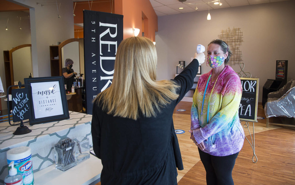 Upon entering, client Pam Junkin gets her temperature checked and then fills out a health questionnaire at Salon Zuberenz in Lynnwood. (Andy Bronson / The Herald)
