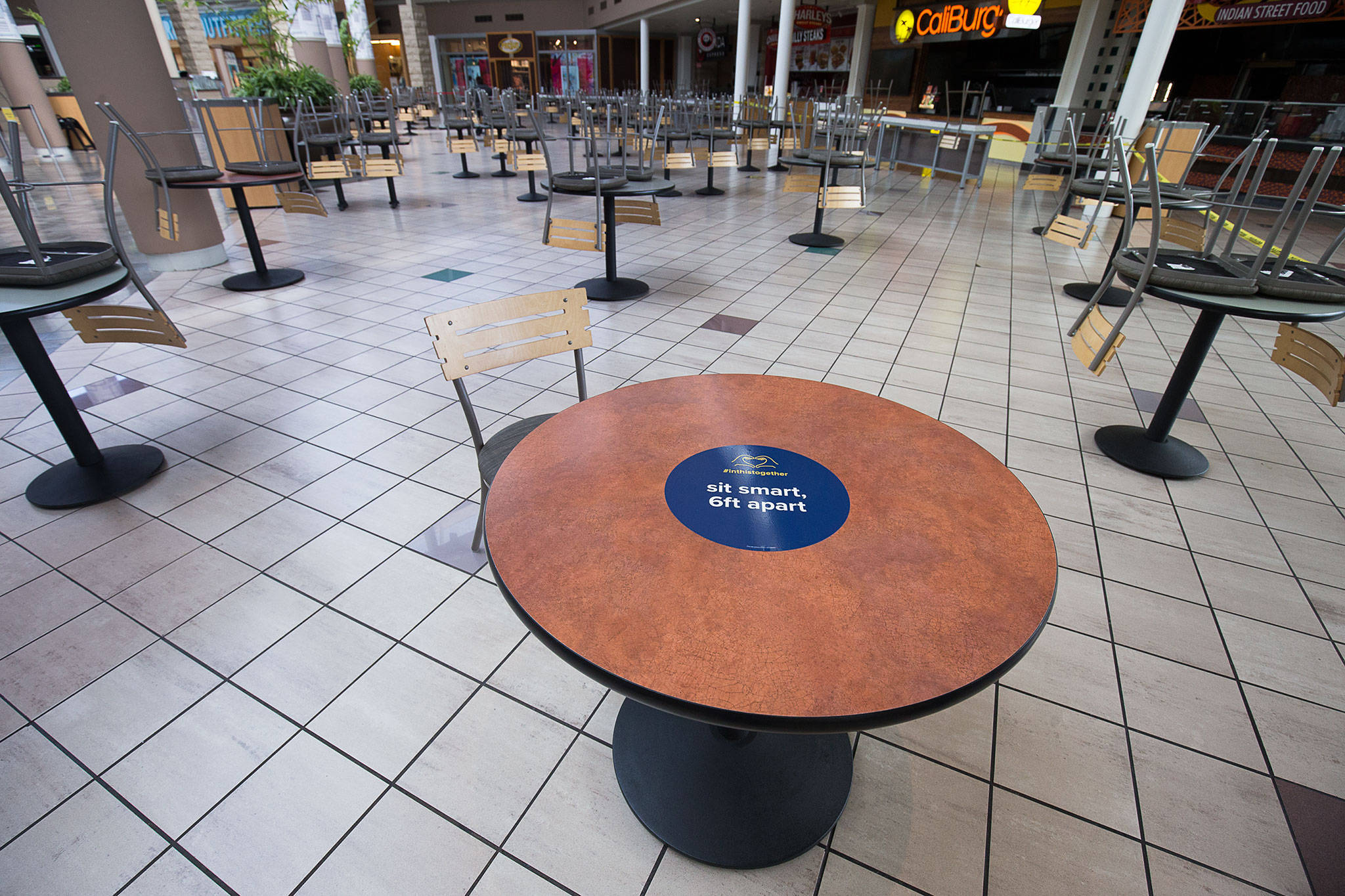 With many tables and chairs already removed for social distancing, a sign in the food pavilion reminds diners to stay apart at the Alderwood mall. (Andy Bronson / Herald file)