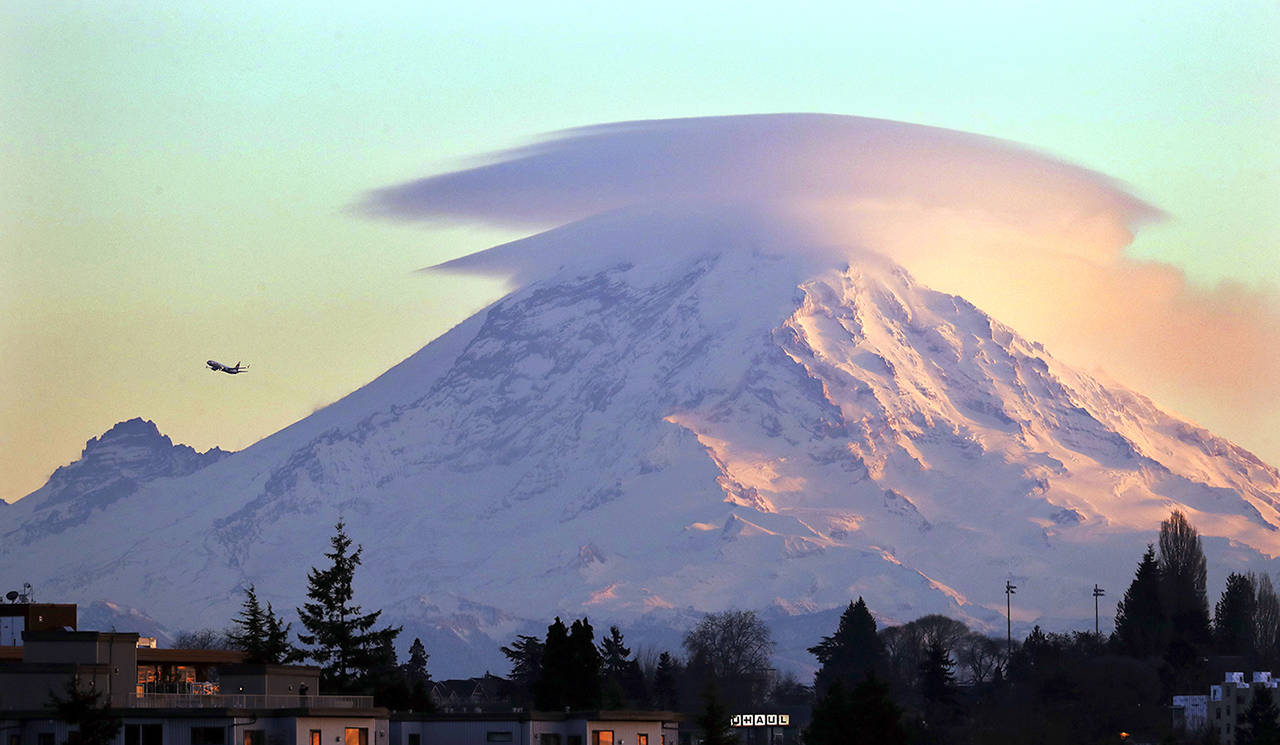 Lenticular clouds cap Mount Rainier, one of Washington state’s premier national parks, at dusk as a jet passes by in December 2018, as seen from Seattle. (Elaine Thompson / Associated Press file photo)
