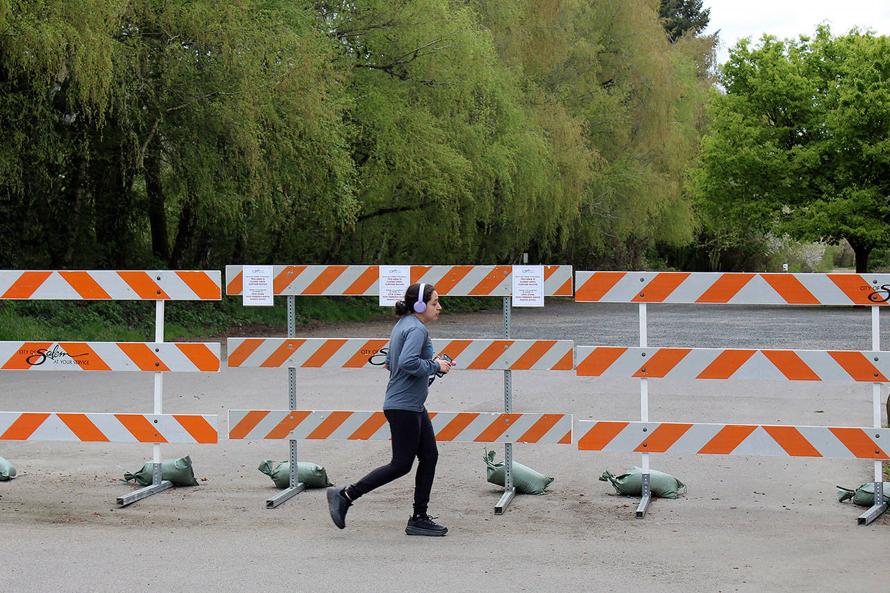 In this April 15 photo, a woman jogs past a barricade outside a park in Salem, Oregon. The state has paused its reopening after reporting its largest daily virus count Thursday. (AP Photo/Andrew Selsky)