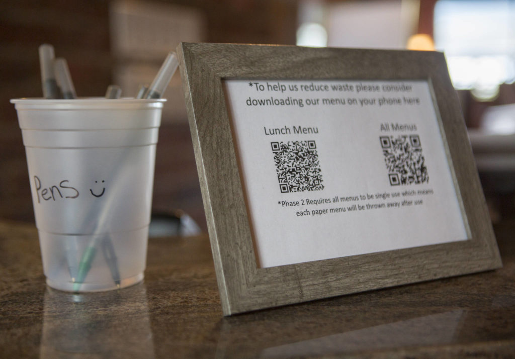 A cup with clean pens and a sheet with a QR code for a virtual menu sit on the host desk at Lombardi’s Italian Restaurant on Saturday in Everett. (Olivia Vanni / The Herald)
