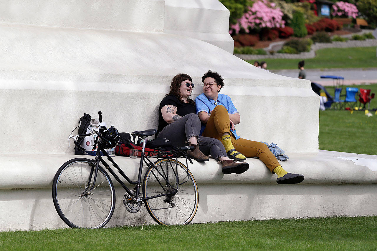 In this May 17 photo, sweethearts Hannah Smith (left) of Vancouver, British Columbia, and Jabree Robinson of Bellingham sit on the base of the Peace Arch as they visit at the border between Canada and the U.S. at Peace Arch Park, in Blaine. (AP Photo/Elaine Thompson, file)