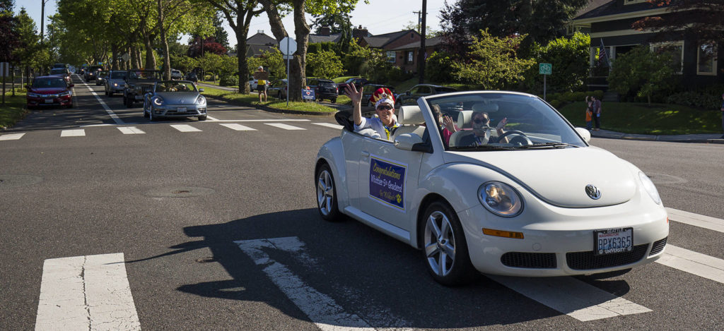 Wearing a crown, music teacher George Spencer waves from a white Volkswagen Bug convertible as the car leads a parade for Whittier Elementary teachers and staff on Wednesday in Everett. Spencer is retiring after 36 years with the Everett School District. (Andy Bronson / The Herald)
