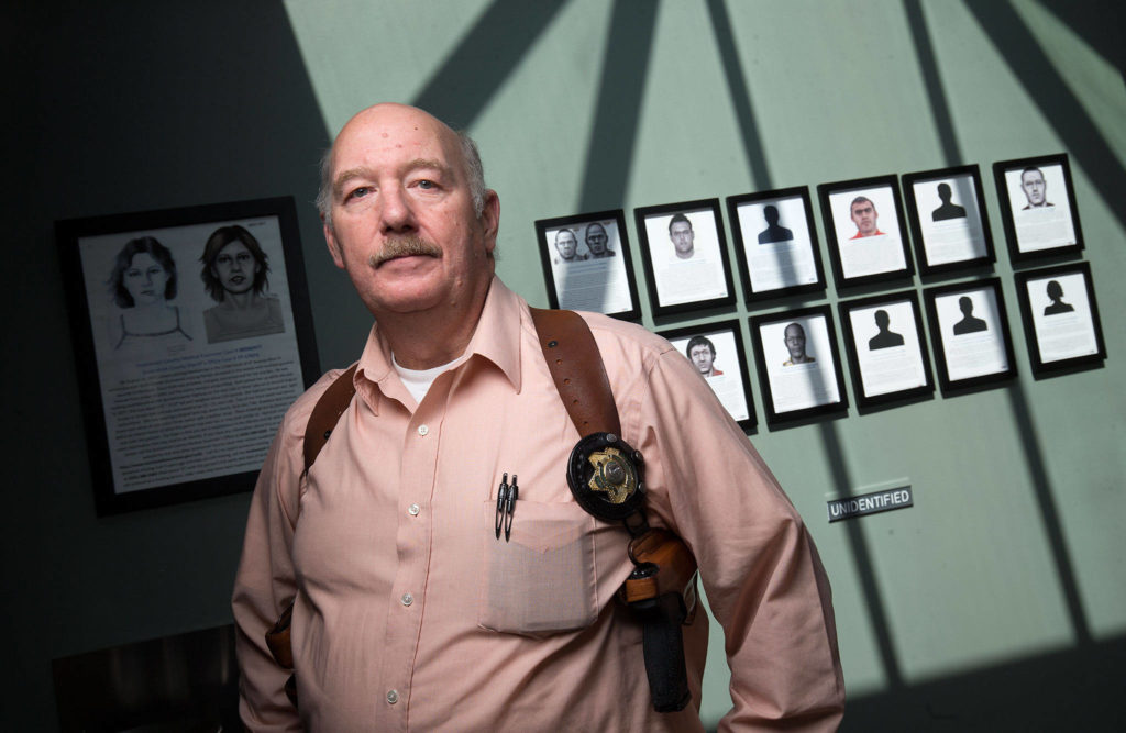 Jim Scharf, a detective for the Snohomish County Sheriff’s Office, stands in front of a display for unidentified persons on a wall at the Snohomish County Medical Examiners Office in 2018 in Everett. Behind his right shoulder is the artist rendering of Precious Jane Doe. (Andy Bronson / Herald file)
