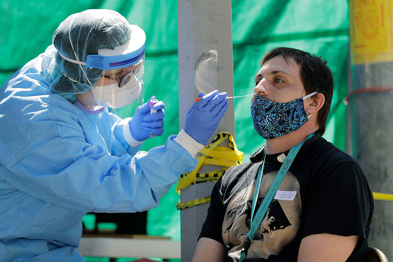 In this May 15 photo, Tina Nguyen (left), a nurse at at the International Community Health Services clinic in Seattle’s International District, takes a nose swab sample from David Carroll, an ICHS employee, during walk- and drive-up testing for COVID-19, in Seattle. (AP Photo/Ted S. Warren)