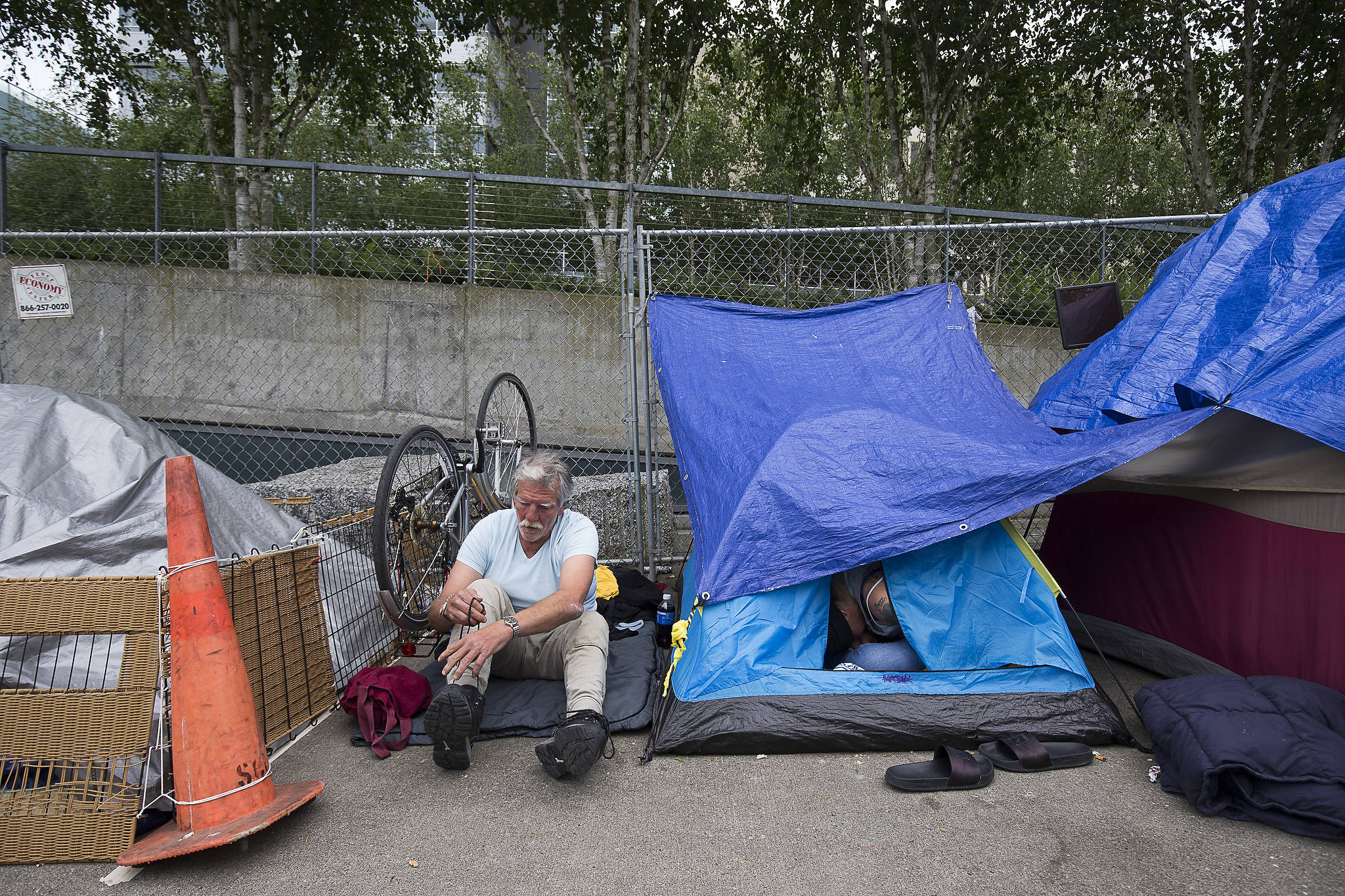 David Curtis puts on shoes at an encampment for homeless people at Wall Street and Oakes Avenue in Everett. (Andy Bronson / The Herald)