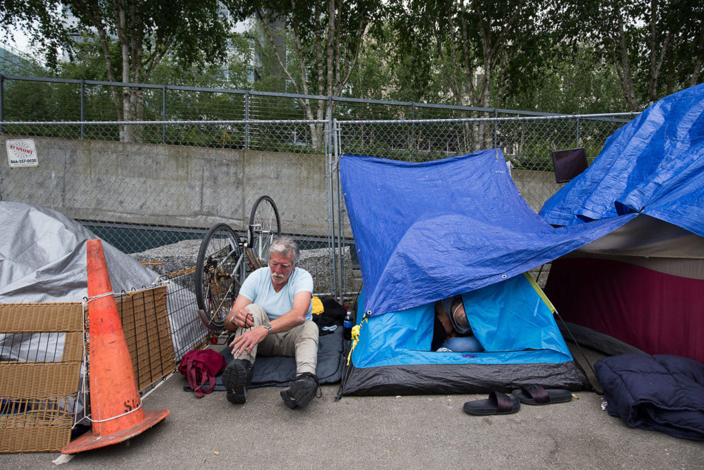David Curtis puts on shoes at an encampment for homeless people at Wall Street and Oakes Avenue in Everett. (Andy Bronson / The Herald)
