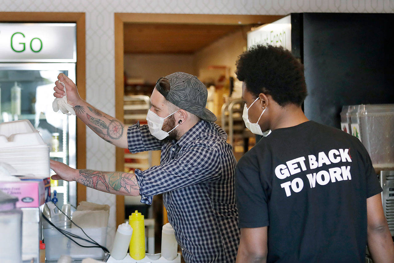Falafel shop workers Bryant Movern (left) and Javohn Ferguson pack take-out orders in a restaurant on May 19 in Seattle. King County has been approved to move into Phase 2 of reopening, which will allow restaurants and taverns to reopen at half capacity with limited table sizes. (AP Photo/Elaine Thompson, file)