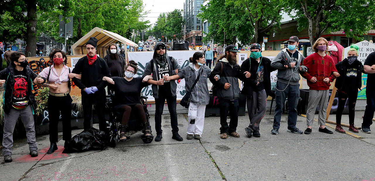 Arms linked, residents of CHOP, the Capitol Hill protest zone, form a human barricade on East Pine Street at 10th Avenue to keep out known people who create problems Saturday in Seattle. (Alan Berner/The Seattle Times via AP)