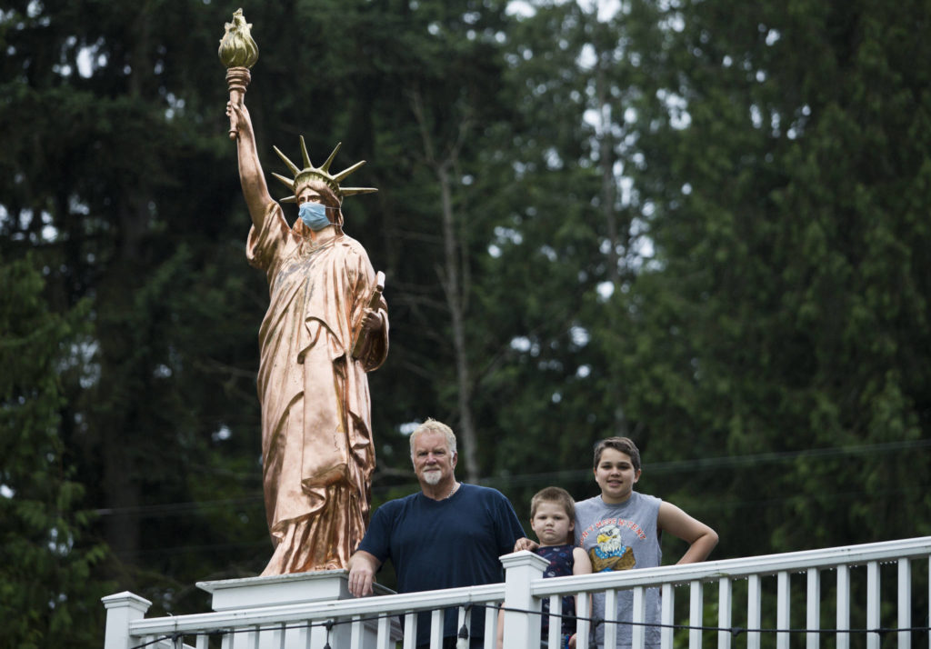 Steve Breeden (left) and his grandsons Otto Medhaug, 6, and Carl Medhaug, 12, next to the large Statue of Liberty replica at his Everett home. Breeden’s statue can be spotted from I-5 and his grandchildren regularly point it out when they drive by. (Olivia Vanni / The Herald)
