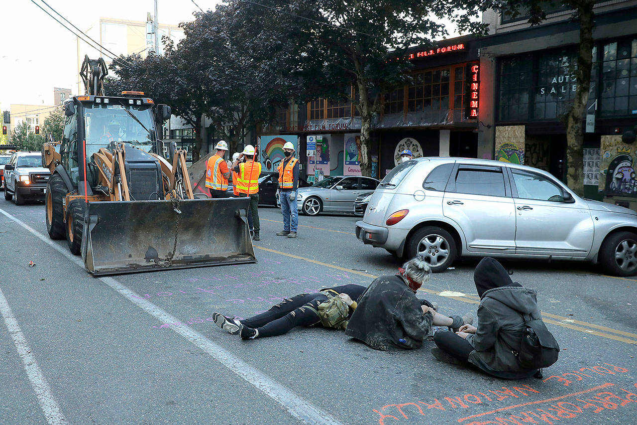 Protesters lie down and sit in the street after workers and heavy equipment from the Seattle Department of Transportation arrived at the the CHOP (Capitol Hill Occupied Protest) zone in Seattle on Friday, with the intention of removing barricades that had been set up in the area. (AP Photo/Ted S. Warren)