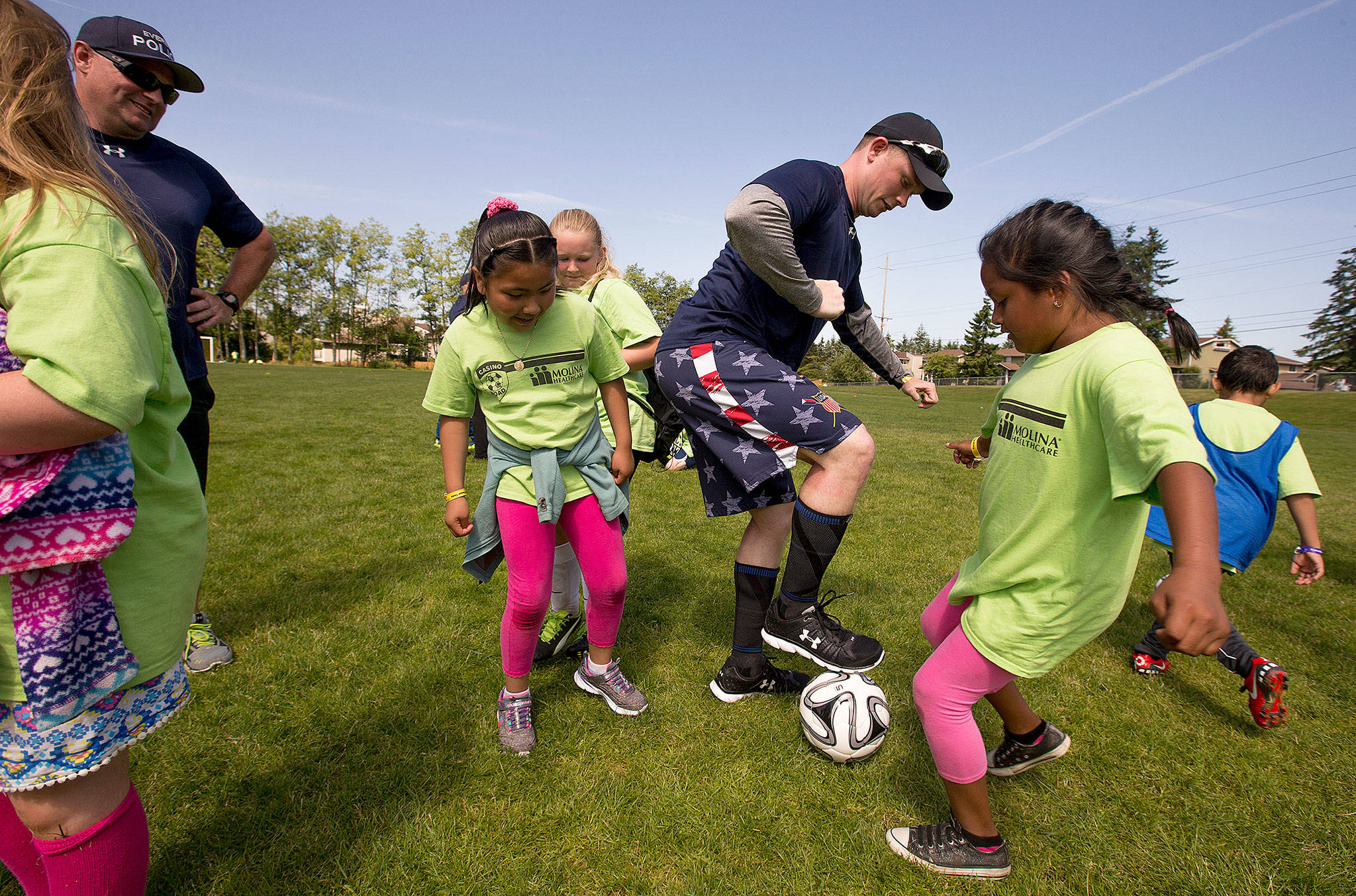 Everett Police Department Recruit John Dorscher tries to keep a soccer ball away from Stephanie Garzon (left) and Ashley Gutierrez-Corona during the Casino Road Futbol Academy held at Walter E. Hall Park on in June, 2017 in Everett. The program is a community outreach effort by the department. (Andy Bronson / Herald file photo)