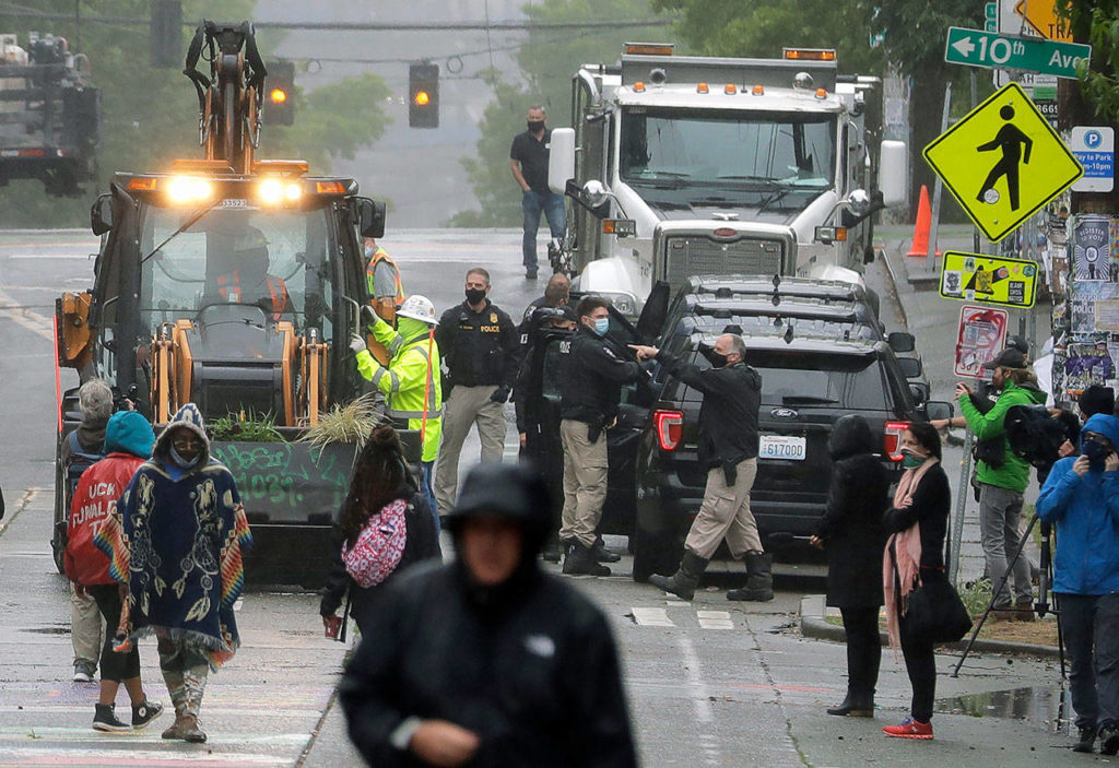 Seattle Police (at right) look on as Department of Transportation workers remove barricades at the intersection of 10th Ave. and Pine St., on Tuesday at the CHOP (Capitol Hill Occupied Protest) zone in Seattle. (AP Photo/Ted S. Warren)
