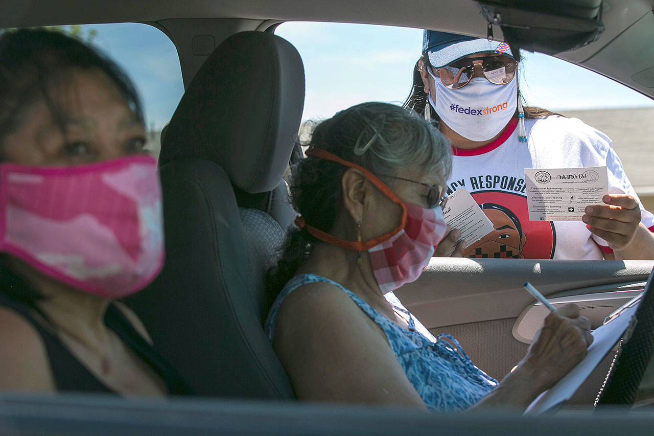 Natasha Scott (right) provides information about the Peacekeeper Society to Patricia Randall (center) and Floraine Gardee during a drive-thru distribution of food and emergency supplies at Harrah City Hall in Harrah, Washington. (Amanda Ray/Yakima Herald-Republic via AP)