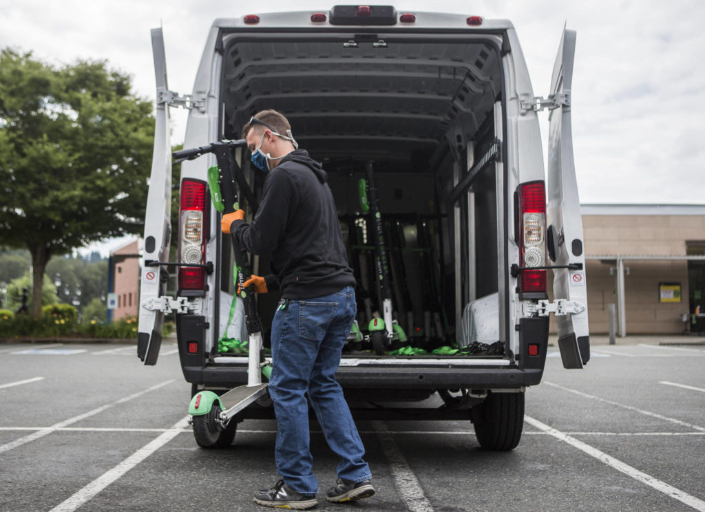 A Lime scooter employee loads scooters in need of charging into a van Wednesday in Bothell. (Olivia Vanni / The Herald)
