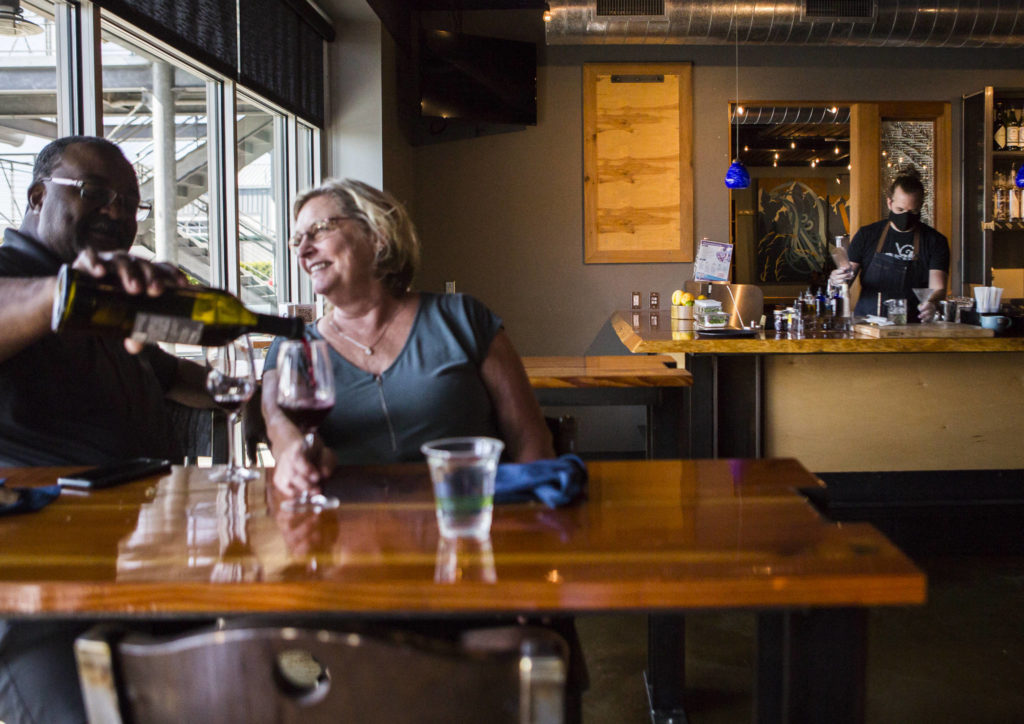 David and Juanita Gibson, left, enjoy a bottle of wine while Kyle Gavin works on cocktail orders Friday at Bluewater Distilling in Everett. (Olivia Vanni / The Herald)
