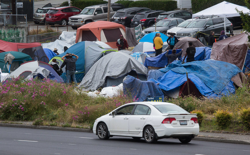 Cars drive by a homeless encampment at 3217 Rucker Ave. on Tuesday in Everett. The camp relocated from the country courthouse plaza. (Andy Bronson / The Herald)
