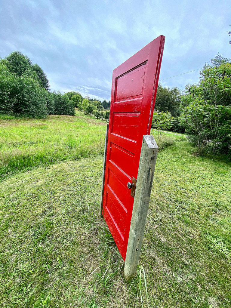 The house on the 17-acre property sits too far to see behind the red door along Cultus Bay Road in Clinton on Whidbey Island. (Andrea Brown / The Herald)
