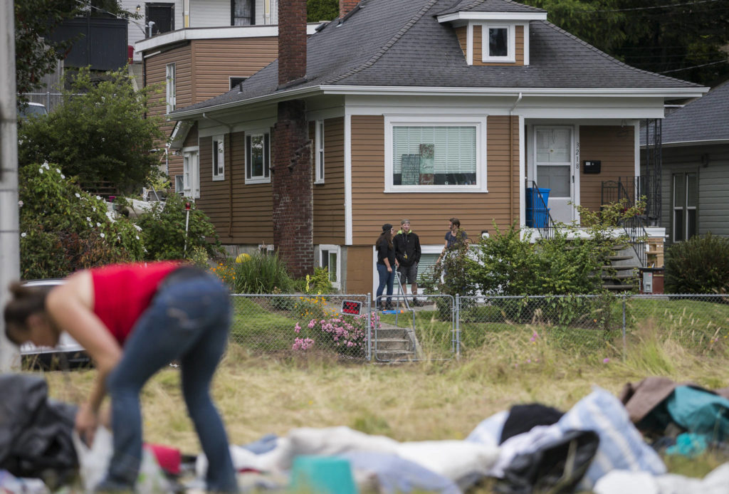 Neighbors watch as people clean and gather their belongings at a homeless encampment on Thursday in Everett. (Olivia Vanni / The Herald) 

