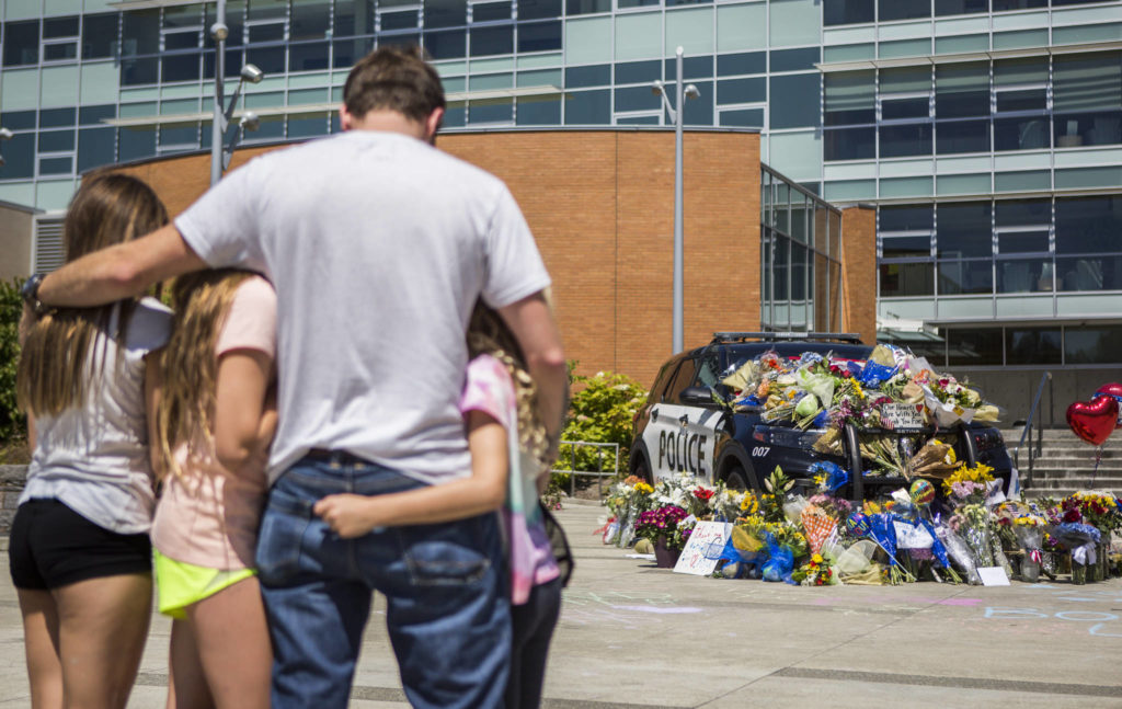 Ryan Murphy holds his daughters, Peyton, Teegan and Paisley, as they pay their respects Tuesday to the Bothell police officer who was killed Monday night. (Olivia Vanni / The Herald)
