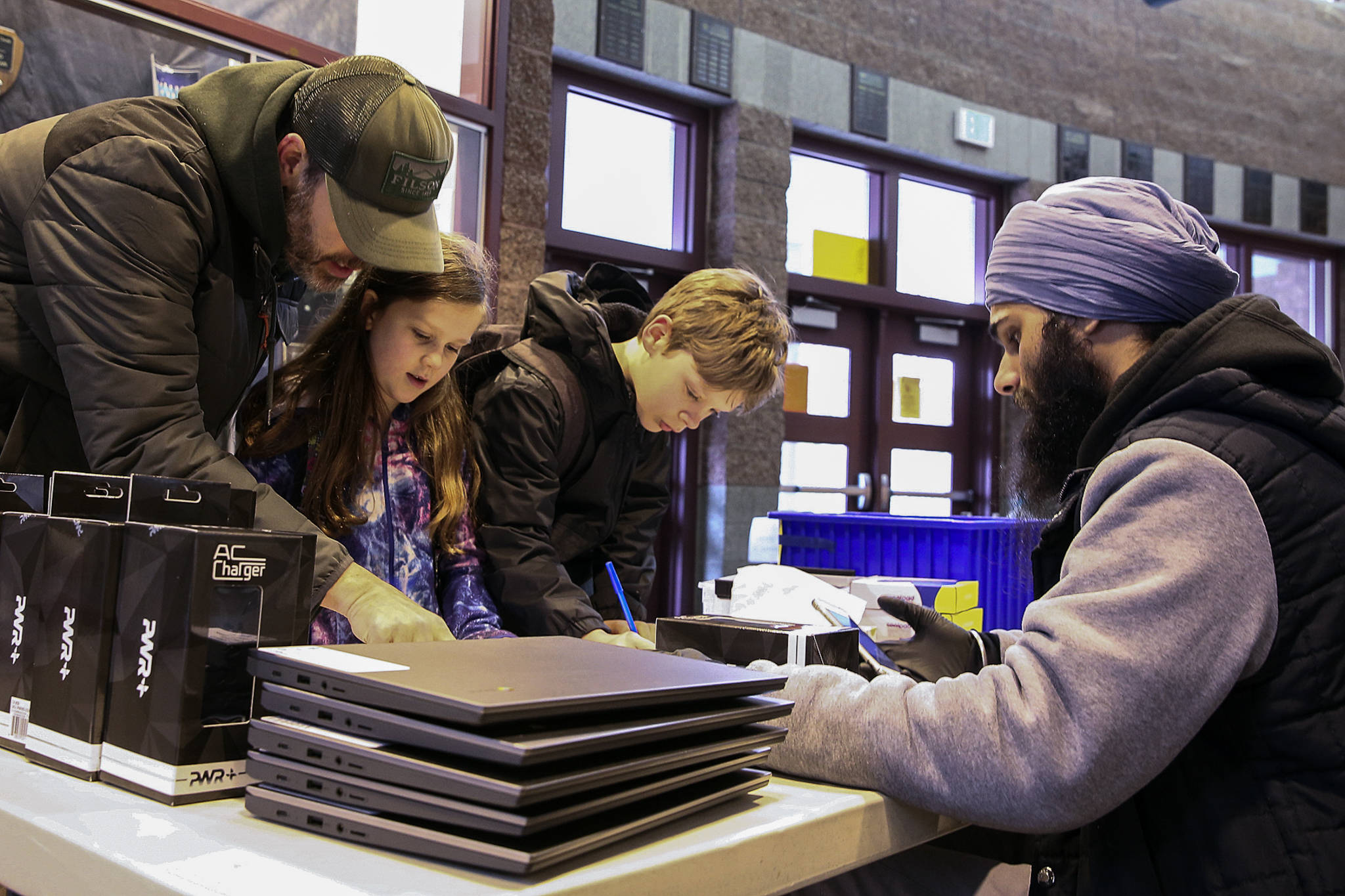 Ryan Hauge (left), Sophia Hauge (center) and Rowan Hauge are assisted by Simran Takhar during check-out of tablet computers in mid-March at Henry M. Jackson High School in Mill Creek. While plans remain under discussion for a return to classes this fall for Everett Public Schools students, district voters are being asked to approve a $317.4 million bond in the primary election that will make improvements throughout the district. (Kevin Clark / Herald file photo)