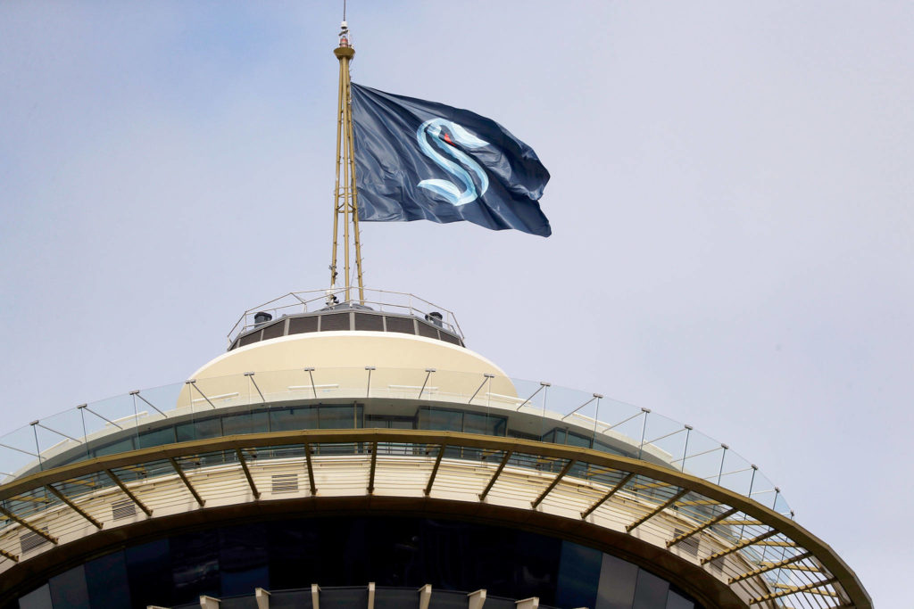 A flag with the new logo for the newly named Seattle NHL team, the Seattle Kraken, flies atop the iconic Space Needle Thursday, July 23, 2020, in Seattle. The hockey expansion franchise unveiled its nickname Thursday, ending 19 months of speculation about whether the team might lean traditional or go eccentric with the name for the league’s 32nd team. Seattle’s colors are a deep dark blue with a lighter shade of blue as a complement. (AP Photo/Elaine Thompson)
