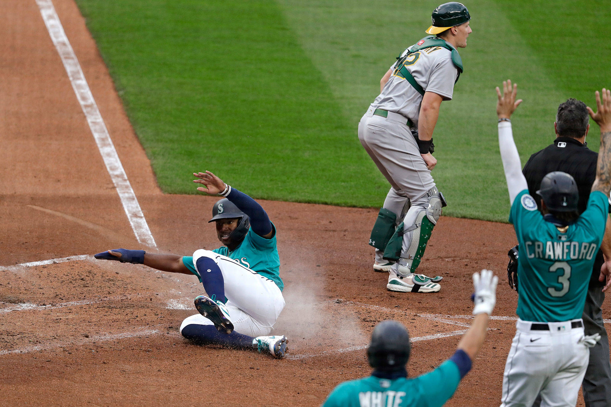 The Mariners’ Kyle Lewis slides safely into home as Athletics catcher Sean Murphy waits for the ball in the fourth inning of a game July 31, 2020, at T-Mobile Park in Seattle. (AP Photo/Elaine Thompson)