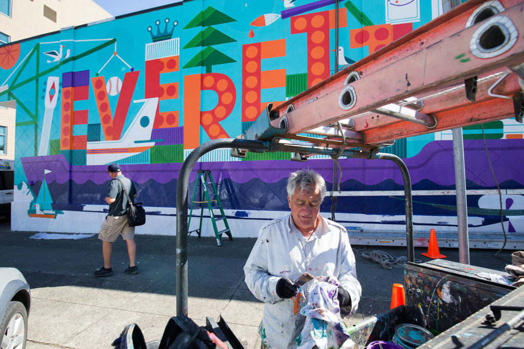 Sign painter Don Rockwell changes out paint brushes as he works on a colorful mural along a wall on California Street on Wednesday in Everett. (Andy Bronson / The Herald)
