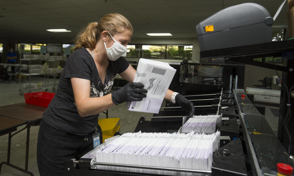 Catherine Berwicks loads ballots into a tray after scanning them at the Snohomish County Elections Ballot Processing Center on Tuesday in Everett. (Andy Bronson / The Herald)
