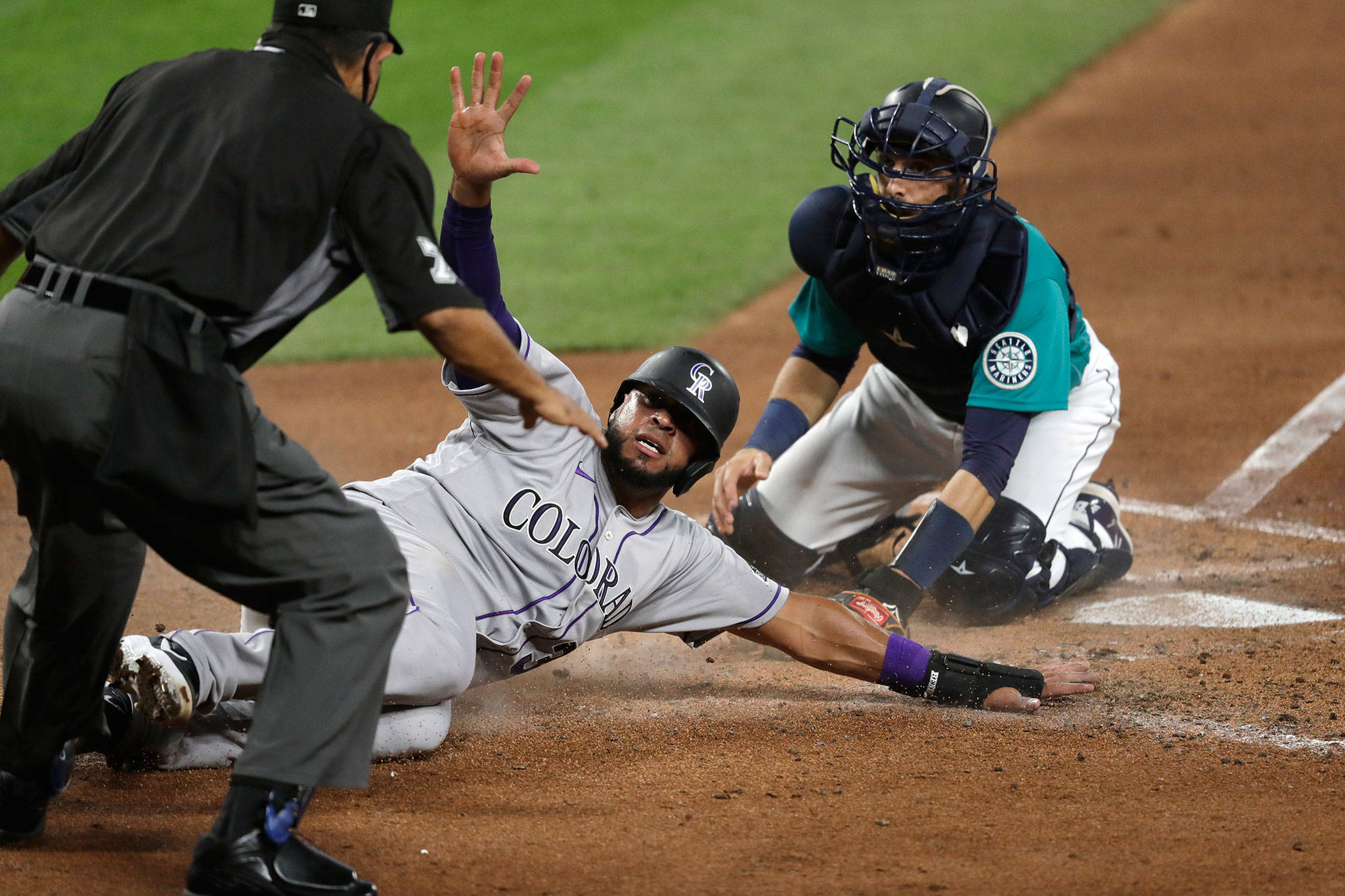 The Rockies’ Elias Diaz and Mariners catcher Austin Nola look up for the call after Diaz safely slid home in the third inning of a game Aug. 7, 2020, in Seattle. (AP Photo/Elaine Thompson)