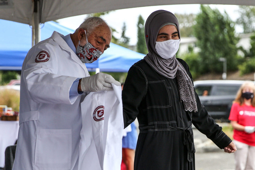 Miriam Al-Saedy has her whitecoat adorned by Larry Schecter, Associate Dean, in the parking lot of the WSU Everett Campus Friday morning on August 21, 2020. (Kevin Clark / The Herald)
