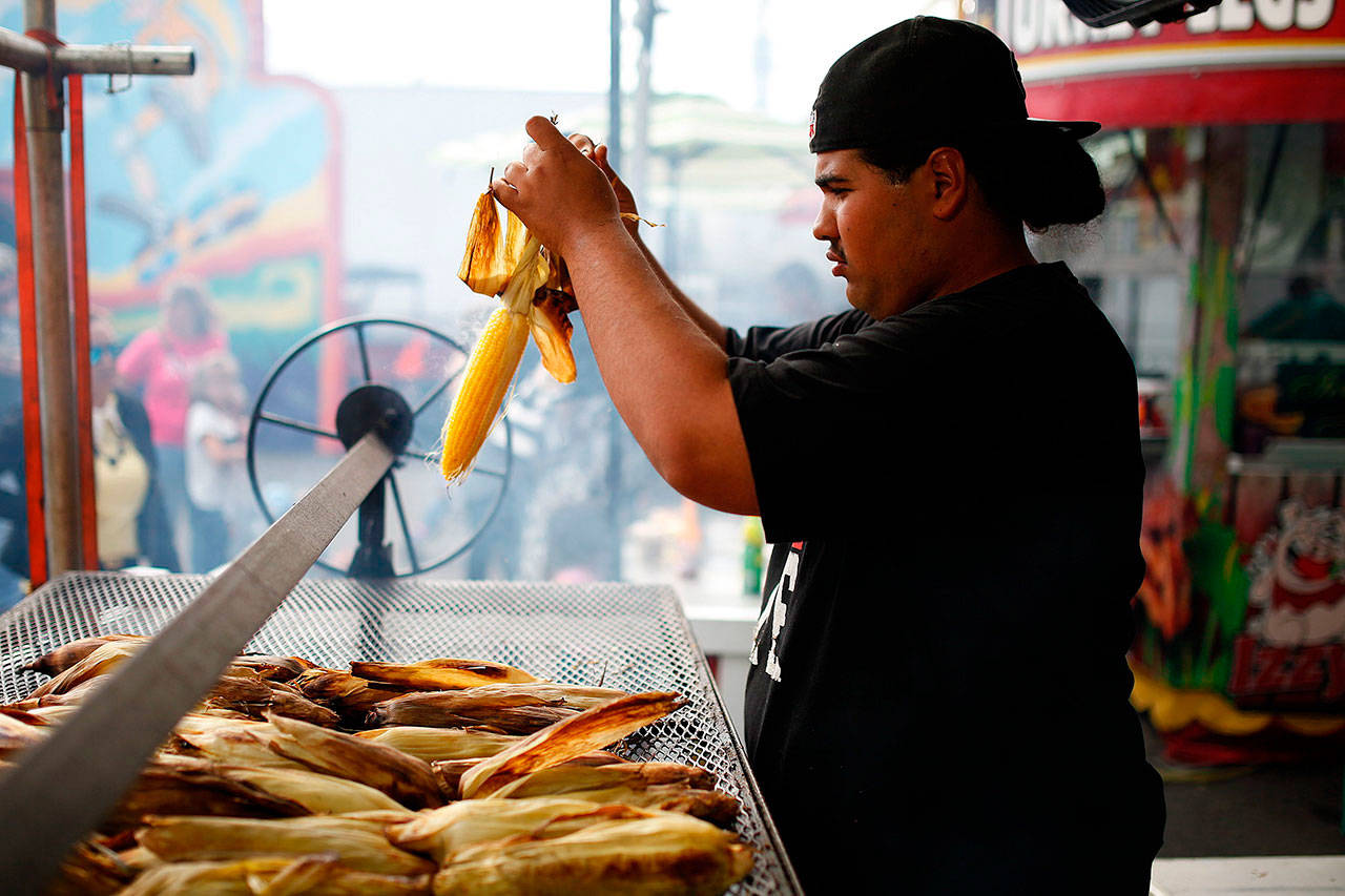Art Rosales prepares an ear of roasted corn for a customer at Izzy’s Barbecue stand at the Evergreen State Fair in Monroe in September 2015. The fair has been cancelled this year because of the pandemic, but a food drive is planned Thursday at the fairgrounds parking lot to help supply local food banks. (Ian Terry / Herald file photo)
