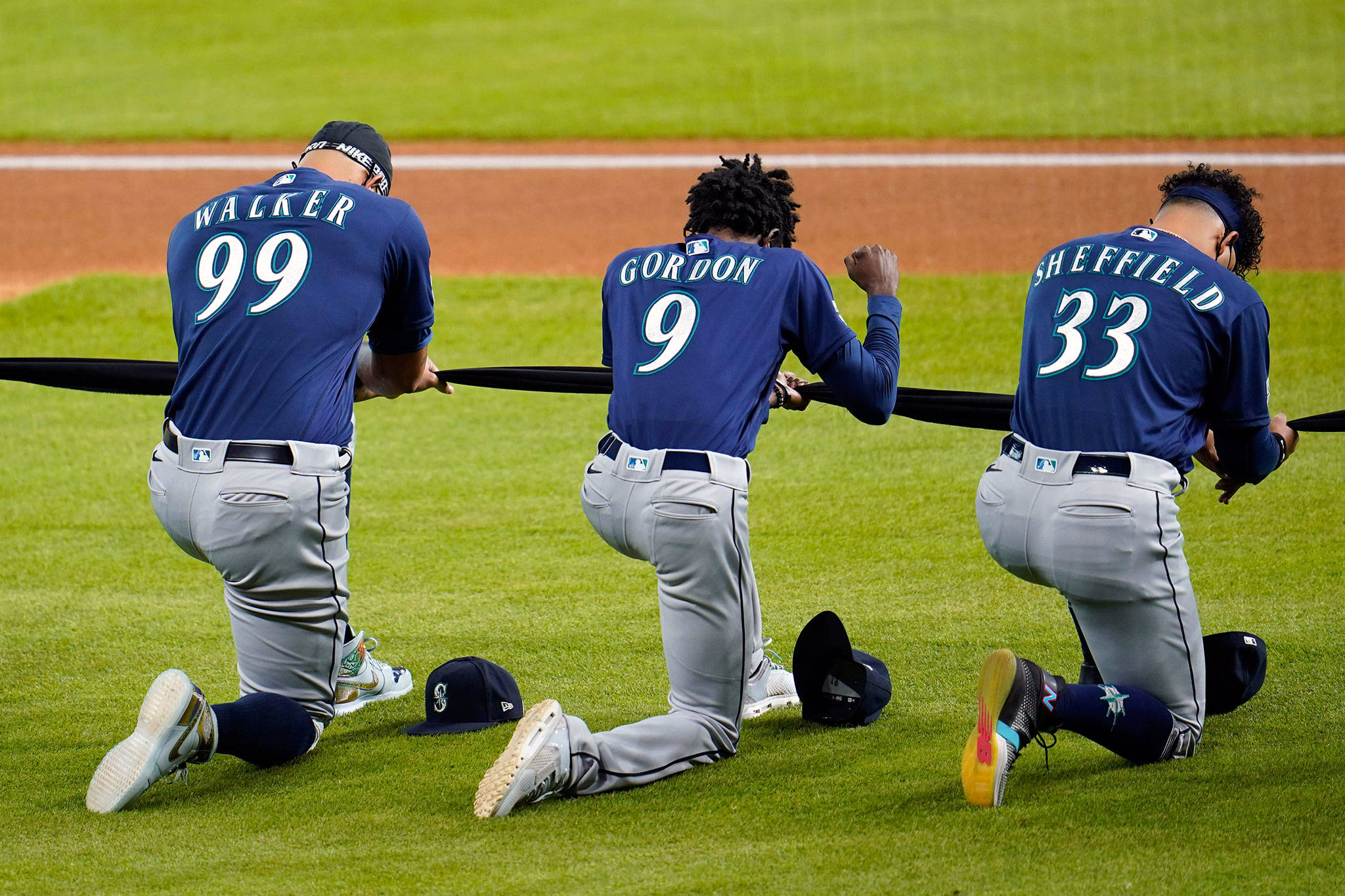 The Mariners’ Dee Gordon (9) raises his fist as he kneels for social justice with teammates Taijuan Walker (99) and Justus Sheffield (33) before a game against the Astros on July 24, 2020, in Houston. (AP Photo/David J. Phillip)
