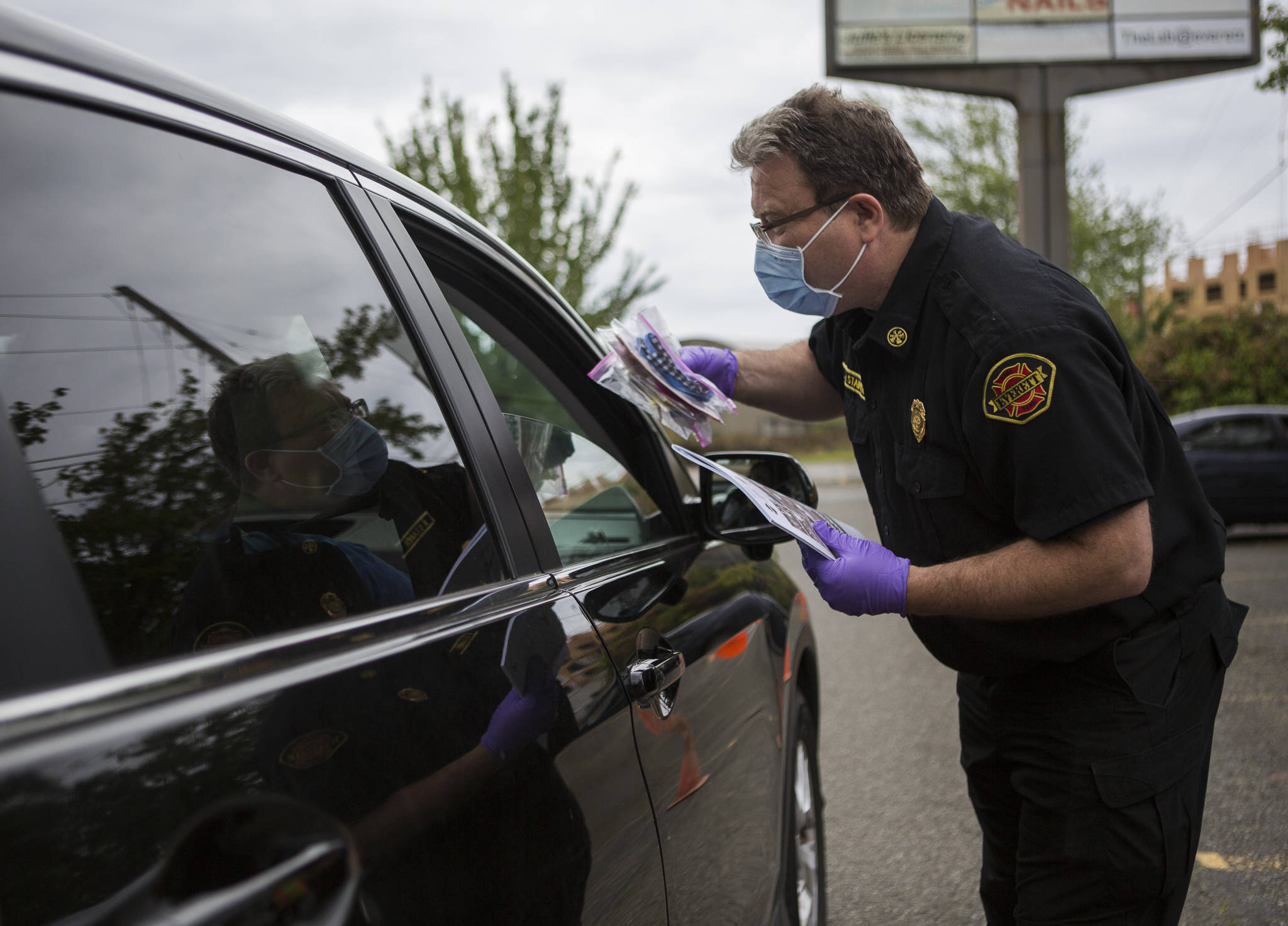 Brent Stainer, director of Emergency Management for the City of Everett, hands out a handful of masks at a free face mMask drive-through at the WSU Everett parking lot in June. (Olivia Vanni / Herald file photo)