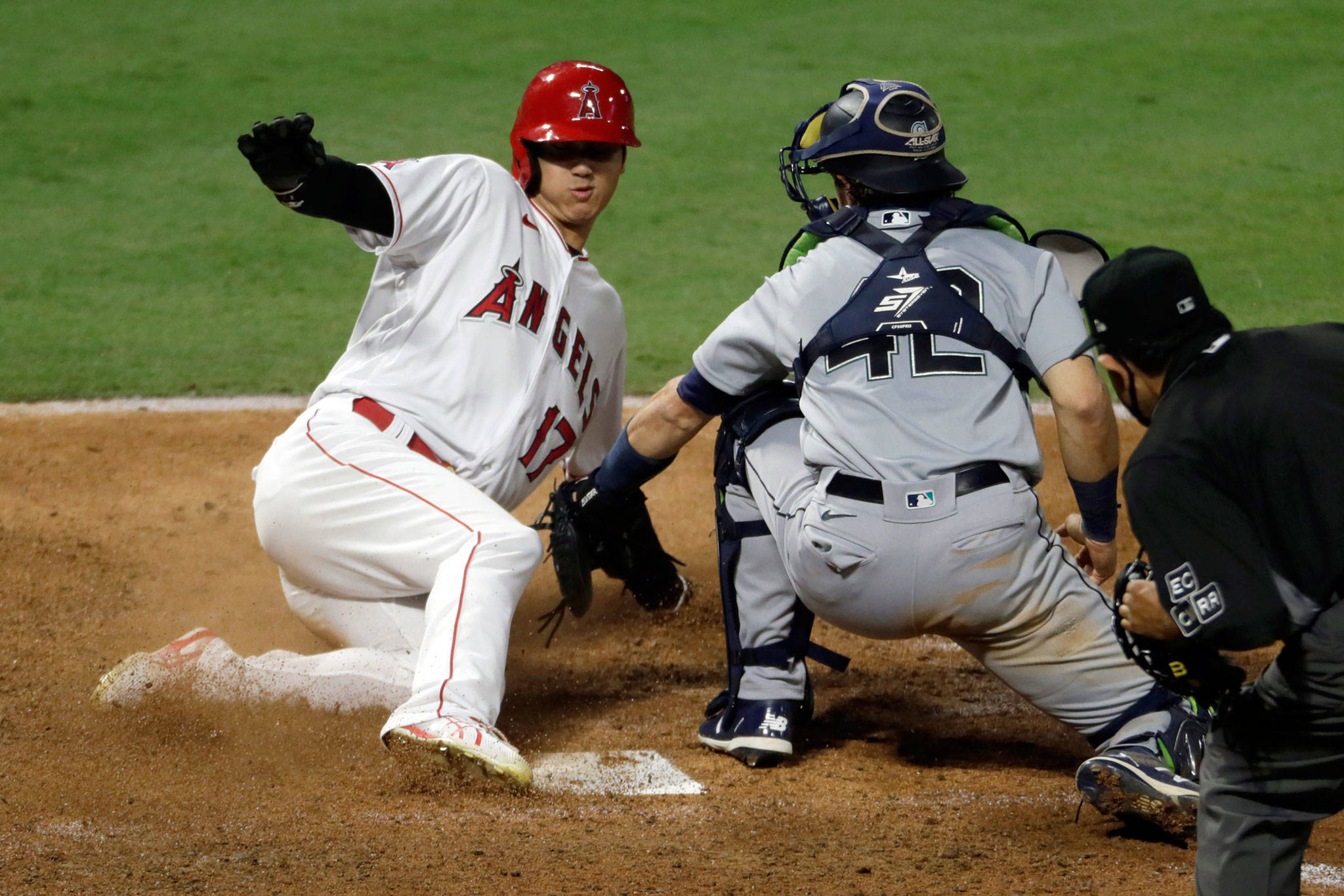 The Angels’ Shohei Ohtani (left) slides into home safely to beat the tag by Mariners catcher Austin Nola on a two-run double by Mike Trout during the sixth inning of a game Aug. 29, 2020, in Anaheim, Calif. (AP Photo/Alex Gallardo)