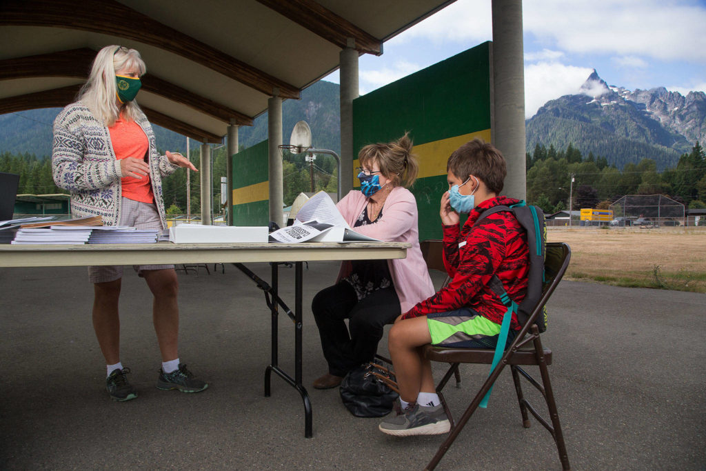 With Whitehorse Mountain looming in the background, Darrington Elementary fifth grade teacher Susan Howard explains how virtual classes will work to Lavinia Bryson and her grandson Bryson Nations outside the school on Tuesday in Darrington. Bryson will be entering the fifth grade. (Andy Bronson / The Herald)
