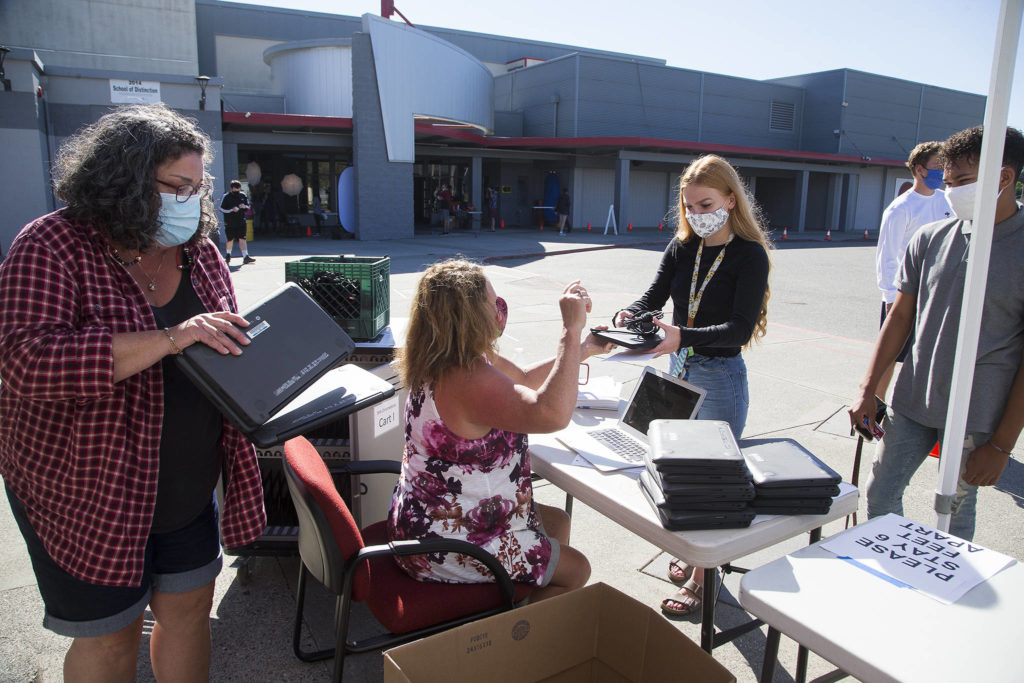 Sheryl Wark stacks computers as Stanwood High’s Renee Herigstad (center) hands a Chromebook to junior Savannah Wickman on Wednesday in Stanwood. Students in the district will be learning online. (Andy Bronson / The Herald)
