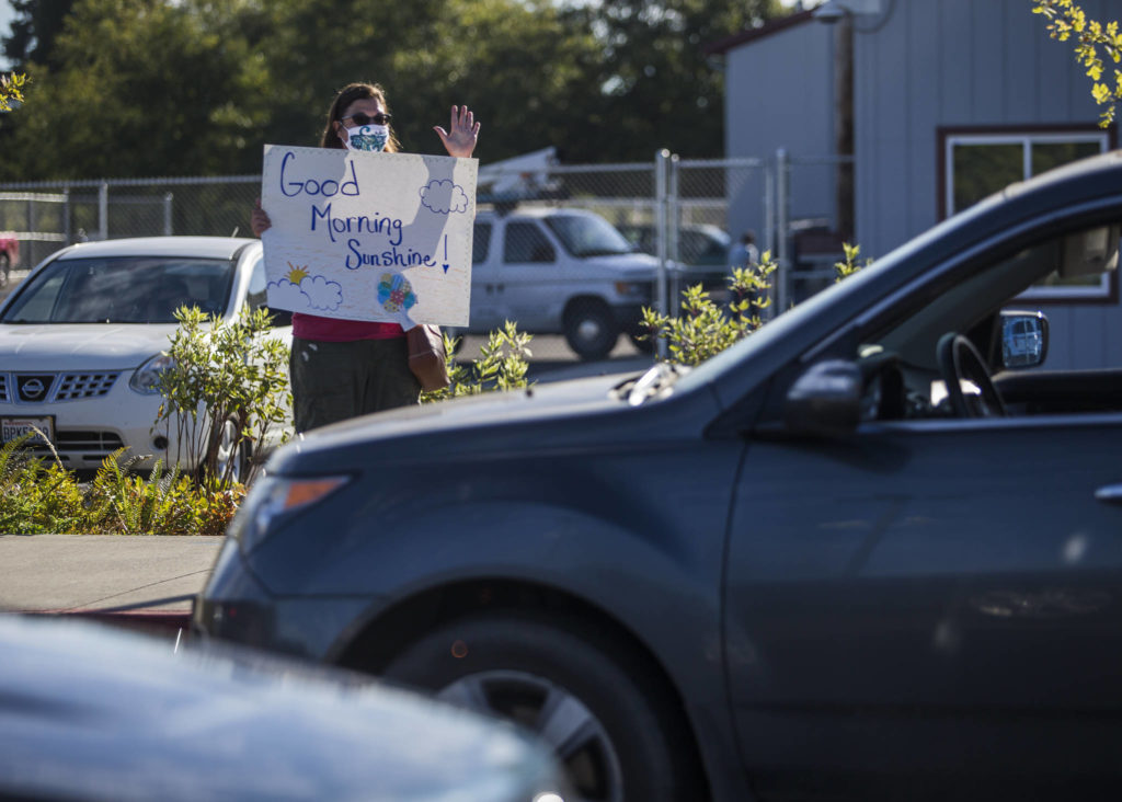 Stanwood High School history teacher Carrie James waves to seniors as they drive by Thursday. (Olivia Vanni / The Herald) 
