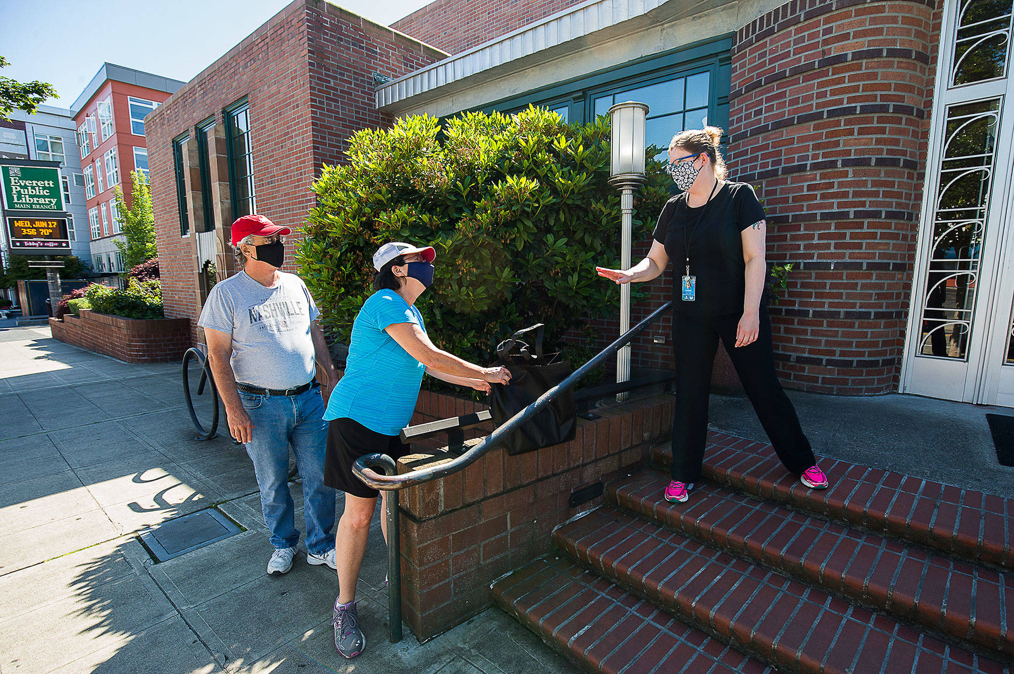 Leslie Bringedahl grabs a bag containing books she and her husband Mark ordered as Circulation Manager Carol puts them down along a wall during curbside pickup at the Everett Public Library in June. Both Everett Public Library and Sno-Isle Libraries are ecnouraging use of library resources even as the buildings remain closed during the pandemic. (Andy Bronson / Herald file photo)
