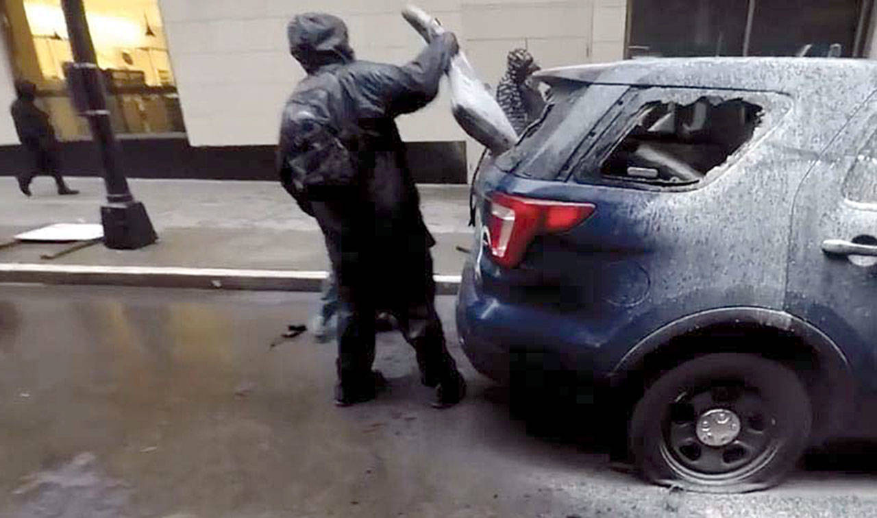 A suspect removes a rifle bag from a broken rear window of a Seattle police car on May 30 in downtown Seattle. An Everett man, Jacob D. Little, 24, has been charged with the theft of the high-powered rifle stolen from the car. This image is from the criminal complaint filed in U.S. District Court.