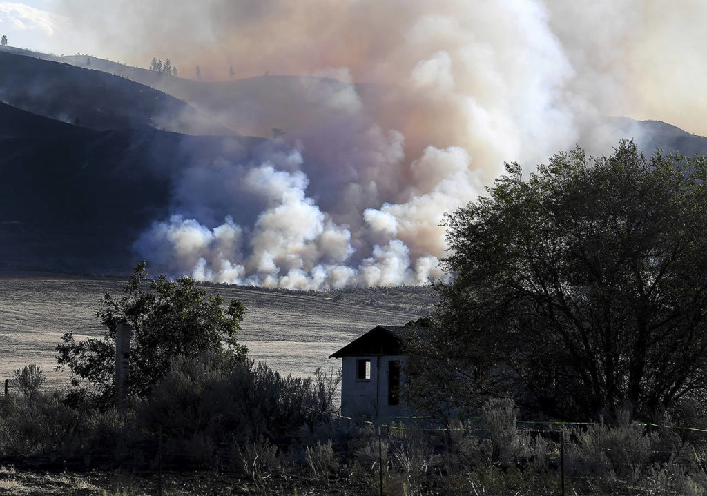 Late afternoon light catches smoke from the Cold Springs Canyon Pearl Hill Fire near a structure that appeared to be empty long before the fire on Monday near Omak. (Tyler Tjomsland/The Spokesman-Review via AP)
