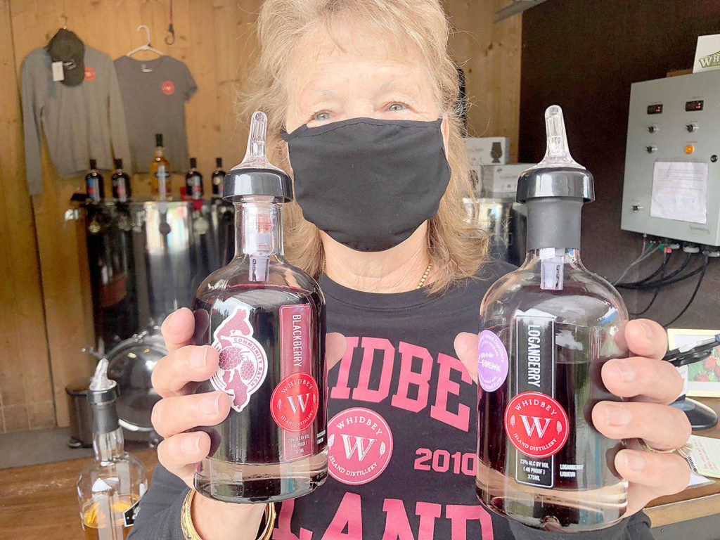 Beverly Heising displays two bottles of Whidbey Island Distillery’s signature liqueurs, which are made from loganberries, blackberries, raspberries and boysenberries. (Emily Gilbert / Whidbey News-Times)
