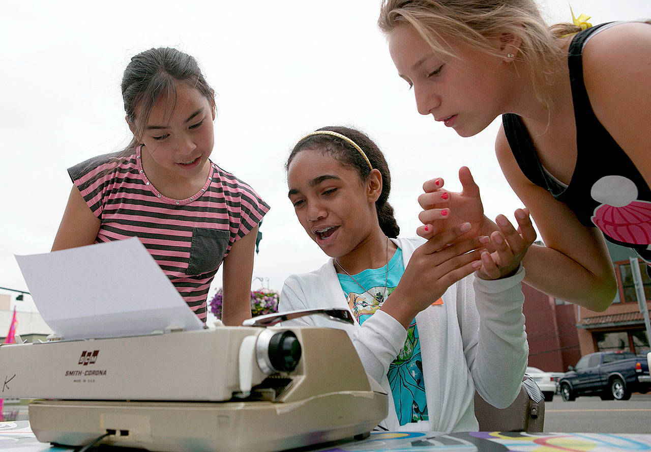 Asianna Smith (center), then 12, of Houston, Texas, attempts to answer the question of the day as Leah Sarles (left), then 11, of Lynnwood, and Hailey Stein, then 11, of Seattle, look on in July of 2014 in downtown Everett. Everett’s “Word on the Street” typewriters weren’t rolled out this summer and are expected to remain on sabbatical next summer as the city considers cuts to its budget. (Kevin Clark / Herald file photo)
