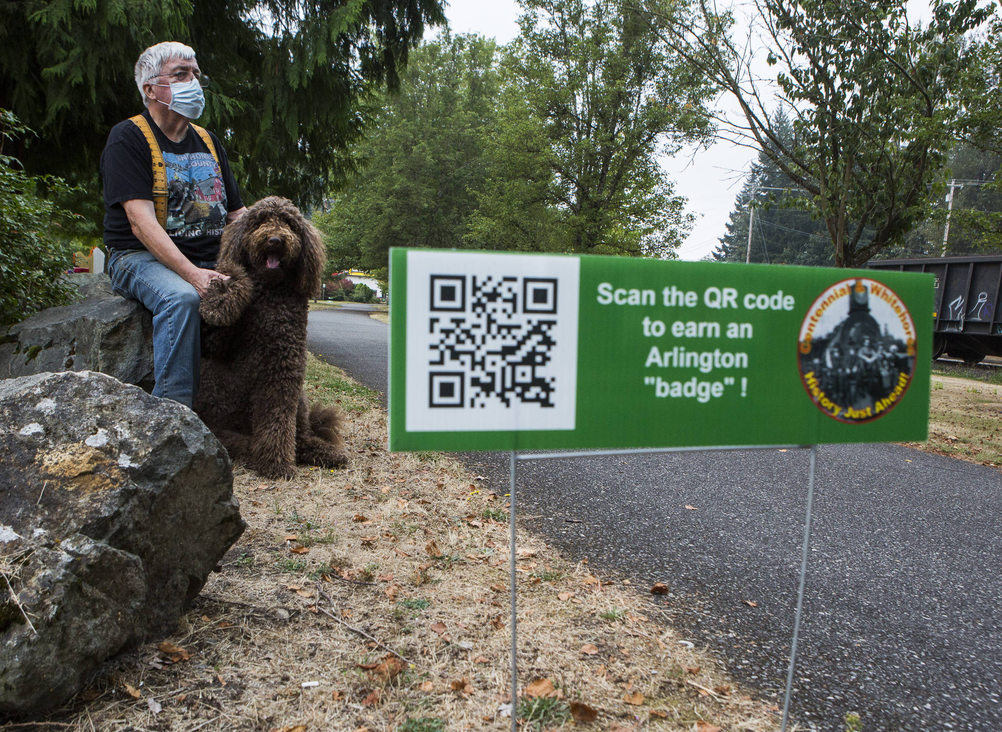 Snohomish Historical Preservation Commission member Fred Cruger with his dog, Duffy, in Arlington along one of the history walk sections at Centennial Trail. The event will be up through September. (Olivia Vanni / The Herald)