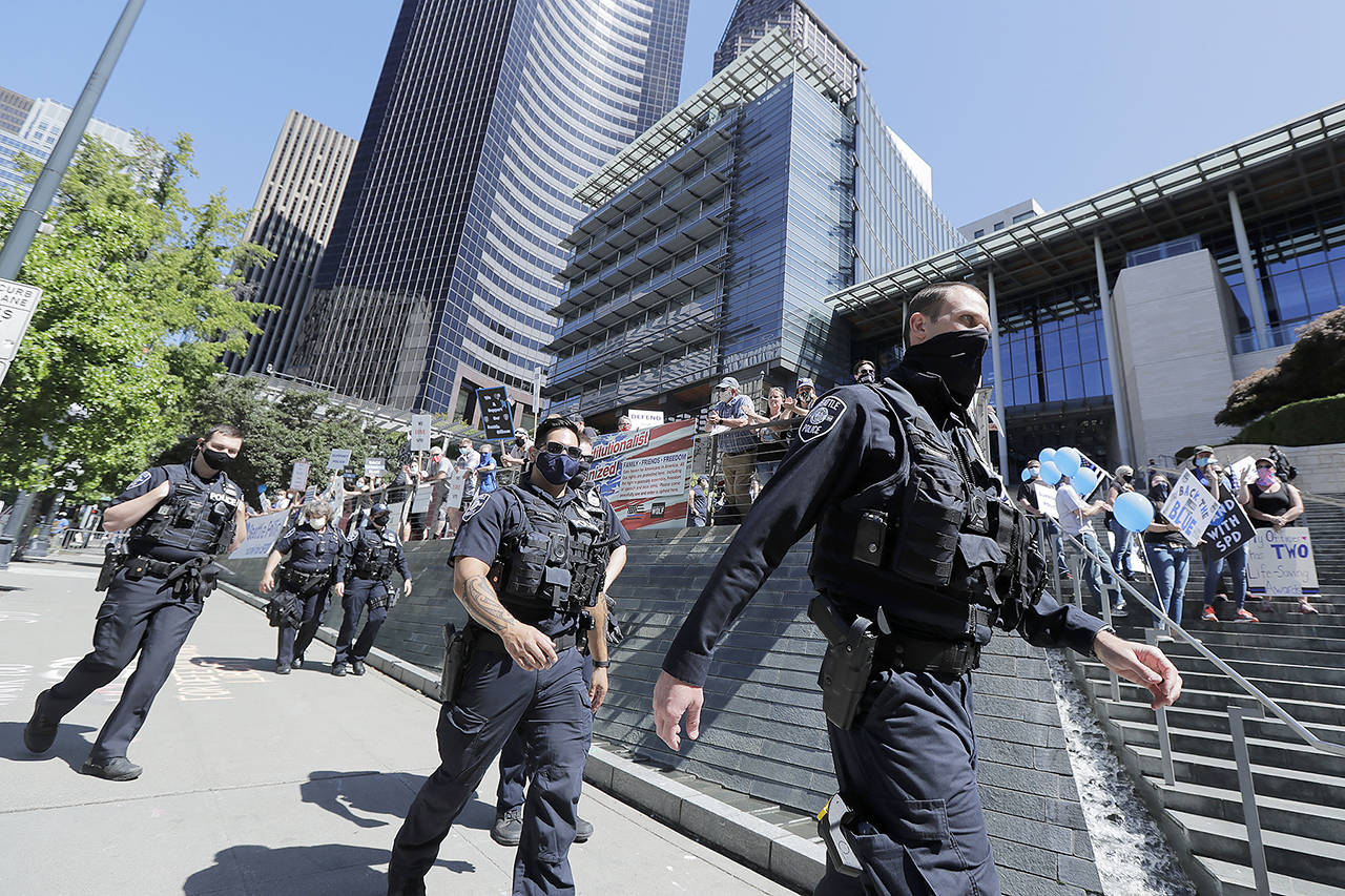 In this July 15 photo, Seattle police officers walk past people holding signs and flags, during a rally in support of police and other law enforcement officers, in front of City Hall in Seattle. (AP Photo/Ted S. Warren, File)