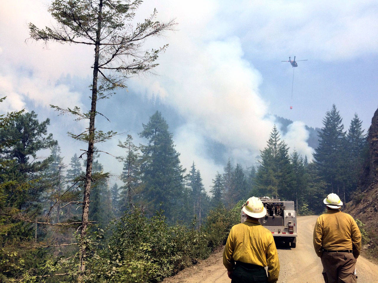 Firefighters approach the Maple Fire in Mason County in 2018 as a helicopter in the distance drops water on the blaze. (State Department of Natural Resources)