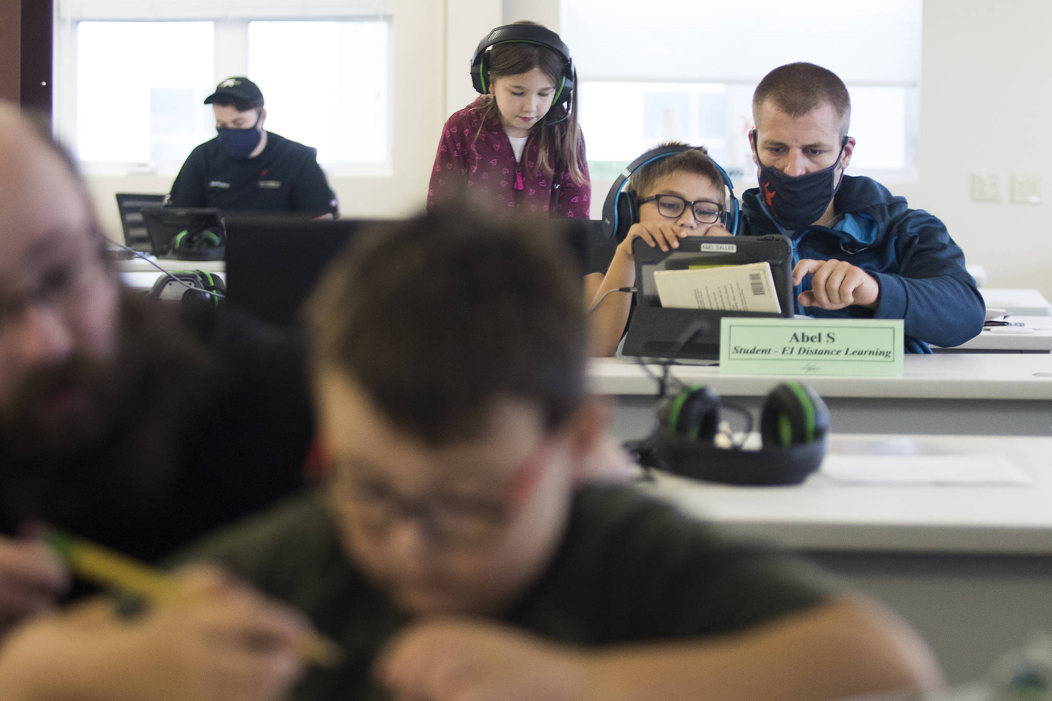 Electroimpact employee Lucas Sallee, right, helps his son, Abel, get connected for Zoom classes before heading to work in another part of the company in Mukilteo. In the foreground, Joel Sanders, works with his son, Joel Jr. (Andy Bronson / The Herald)